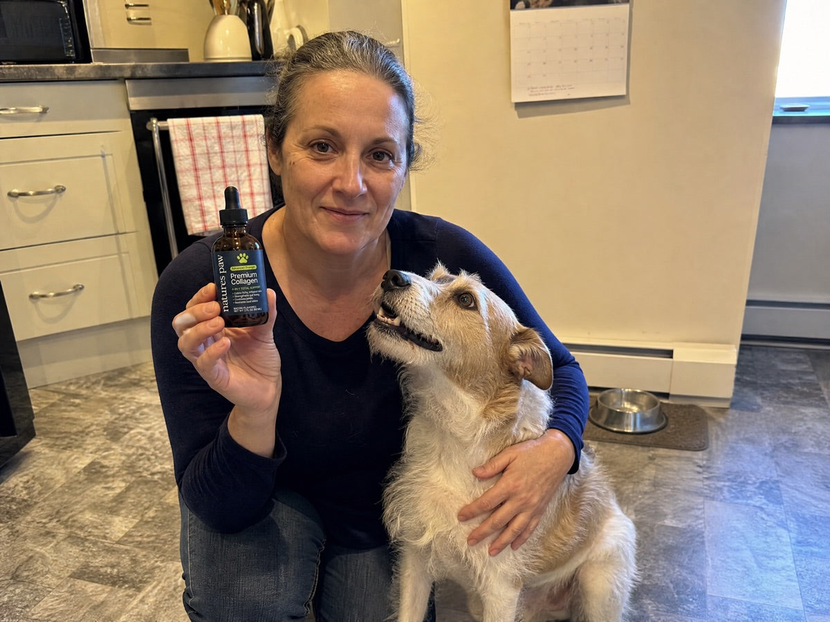 Owner crouched on her kitchen floor holding the navy Nature's Paw bottle, one arm round a scruffy terrier